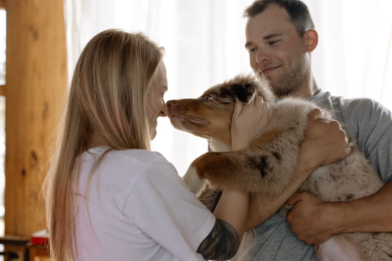 Coppia che coccola il proprio cane in casa con luce naturale e toni caldi